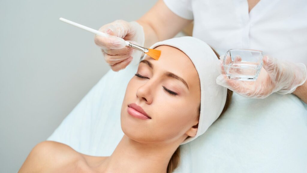 Woman receiving a chemical skin peel treatment from a professional using a brush.