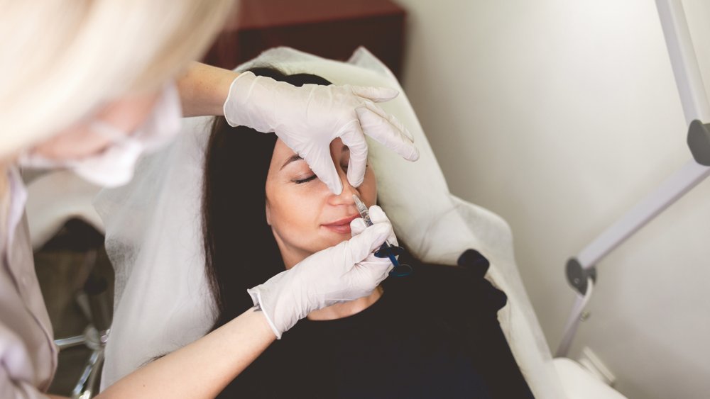 Woman receiving non-surgical nose filler treatment administered by a professional in a clinical setting.